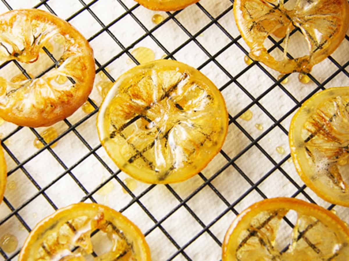 Golden candied lemon slices cooling on a wire rack for dessert garnish.