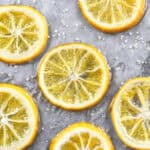 Close-up of candied lemon slices on a gray surface with sugar crystals.