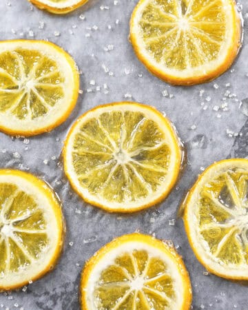 Close-up of candied lemon slices on a gray surface with sugar crystals.