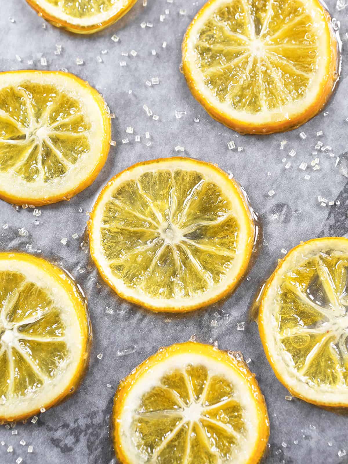 Close-up of candied lemon slices on a gray surface with sugar crystals.