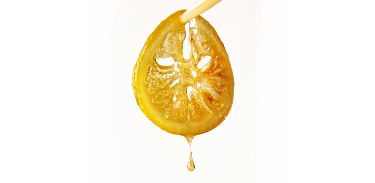 Close-up of a candied lemon slice with a glaze drop on a white background.