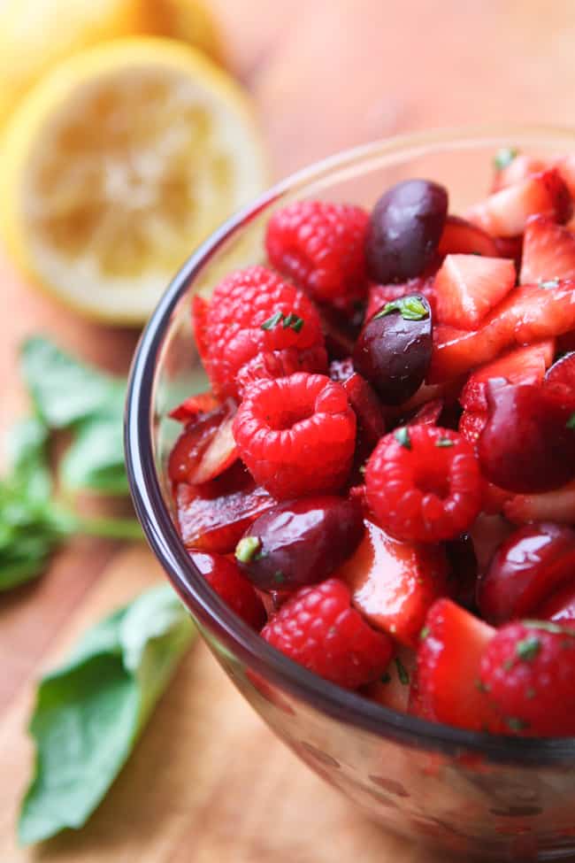 Close up of a bowl full of red fruit salad and a lemon in the background