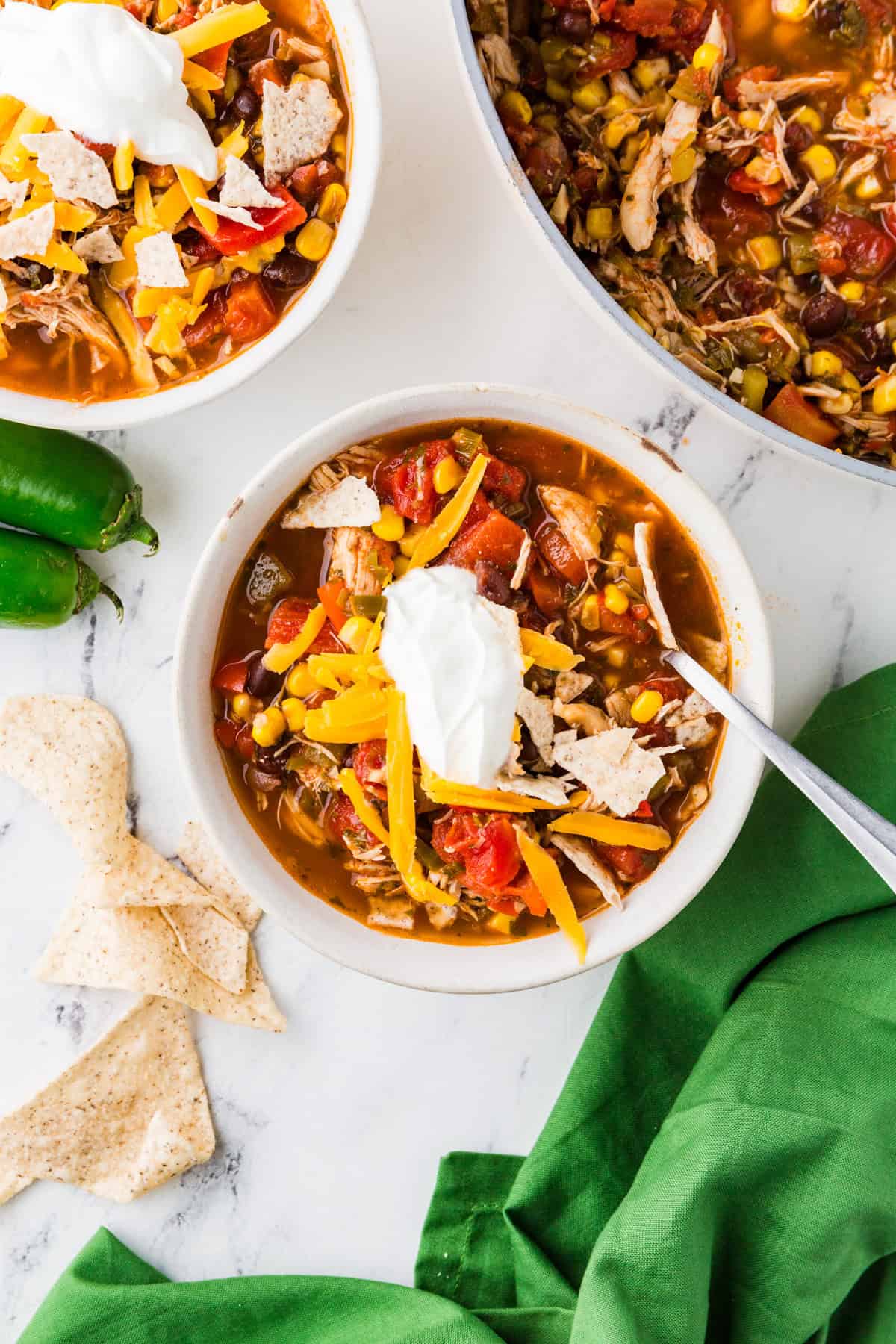 Top view of a bowl of taco soup loaded with toppings and next to another bowl and pan with mixture inside.