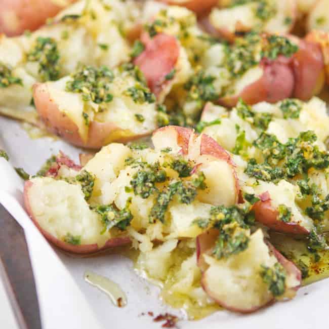 Smashed potatoes with garlic and butter on top on a baking sheet. 