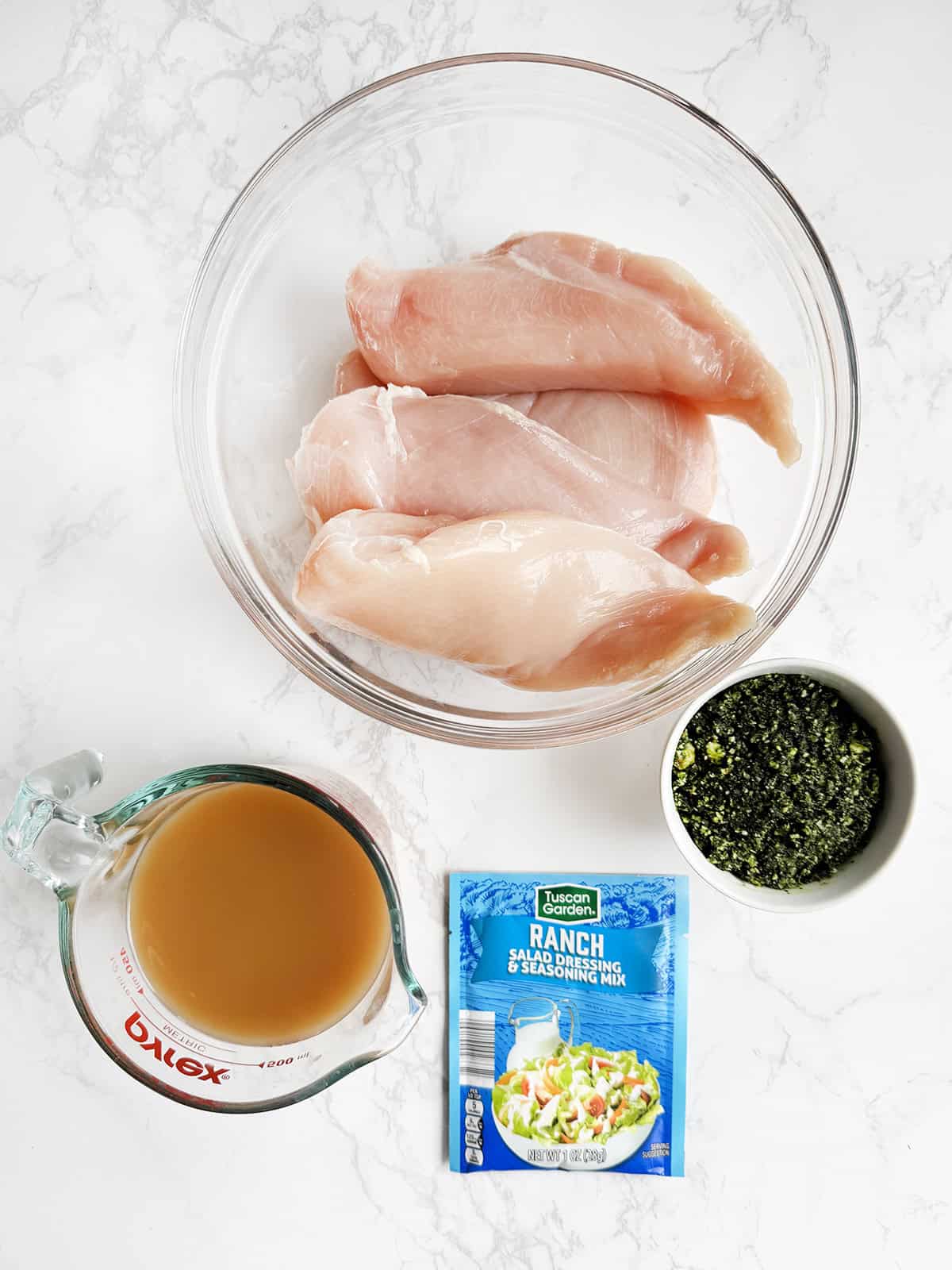 Four ingredients on a white counter, ready to make pesto ranch chicken.