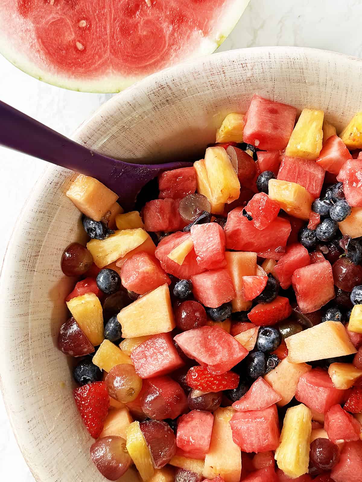 Looking down into a giant bowl of fruit salad, sitting next to a watermelon.