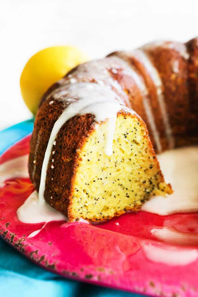 Partial view of a lemon poppyseed cake with a glaze on top and a slice cut out.