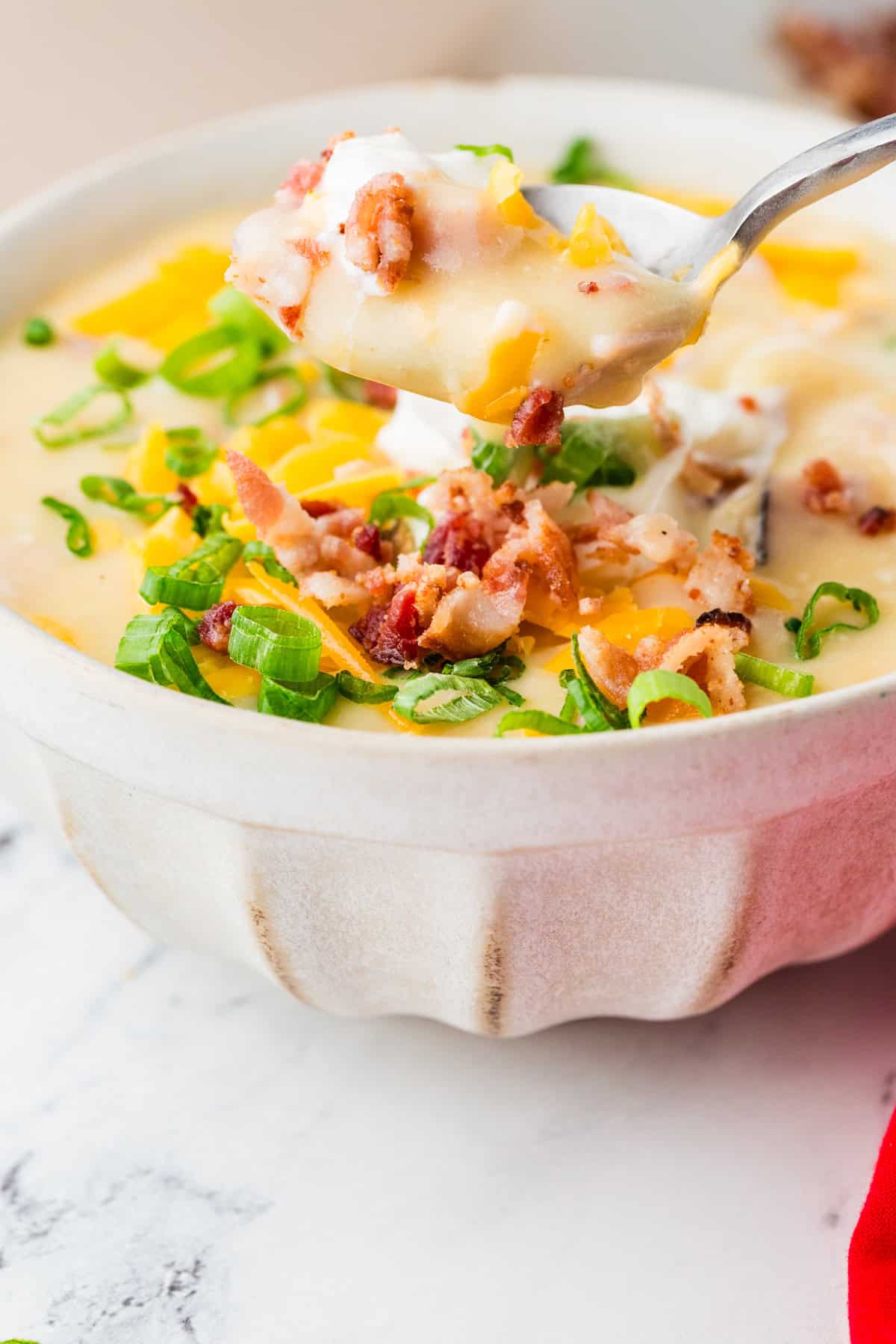 Spoon lifting a bite of soup out of a bowl filled with loaded baked potato soup.