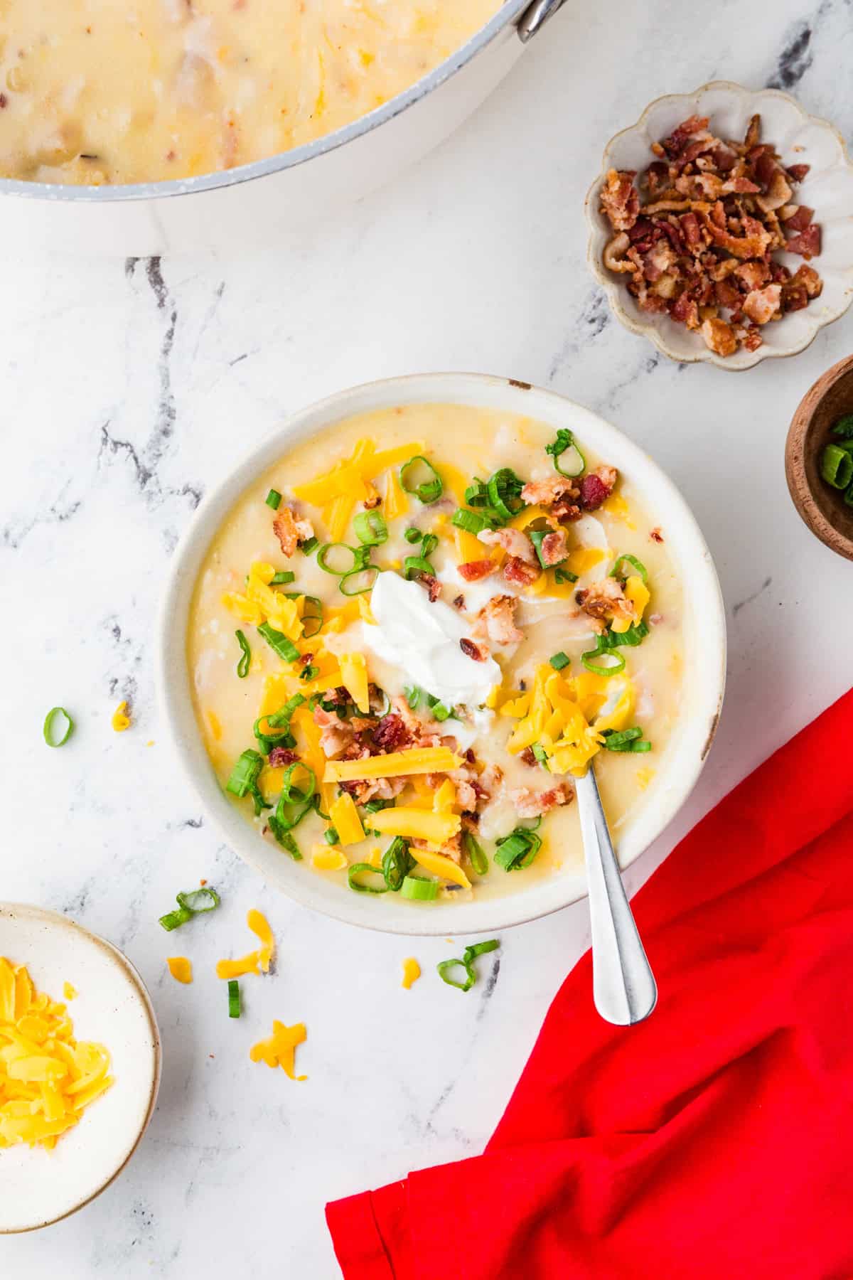 Top view of a bowl of loaded potato soup with toppings in bowls surrounding it.