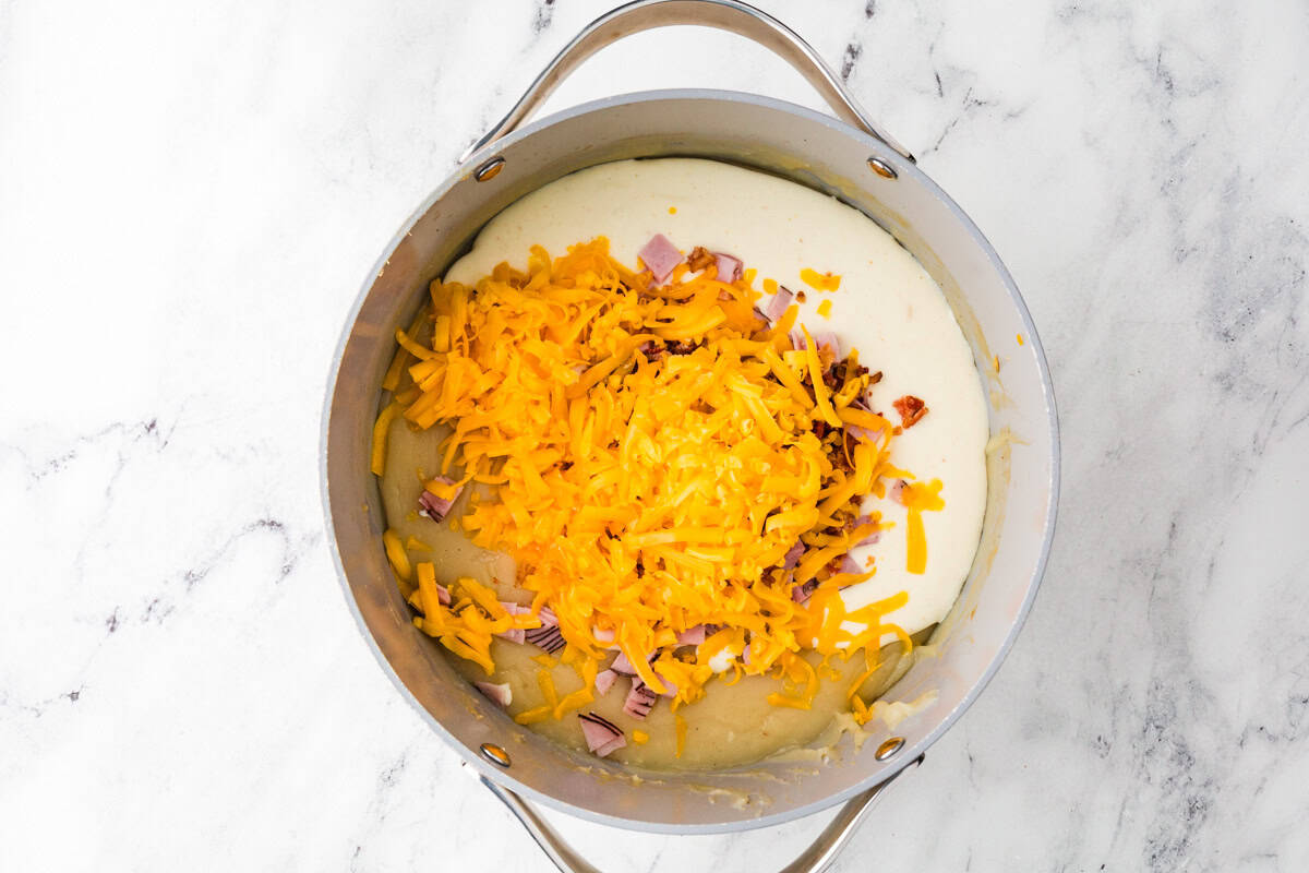 Saucepan with creamy soup, cheddar cheese and bacon pieces.