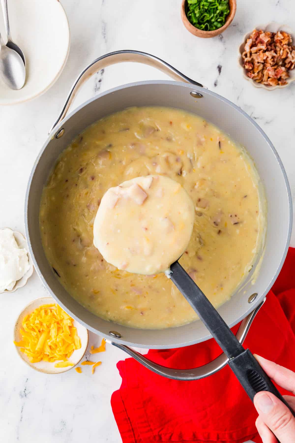 Ladle pulling a scoop of potato soup out of a large pan.
