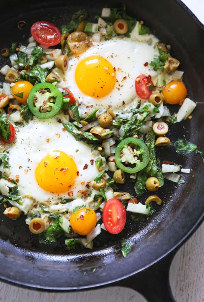 A skillet with veggies and over easy eggs. 