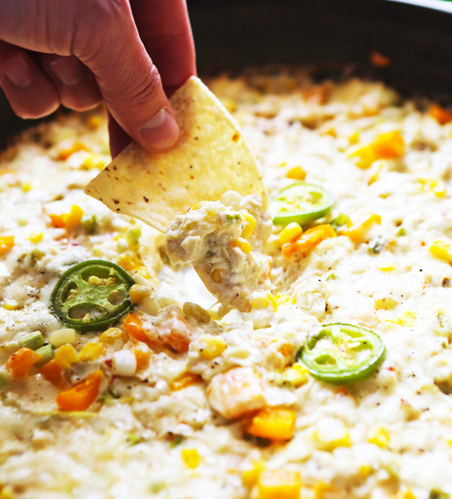 Hand scooping up hot crab dip with a tortilla chip. 