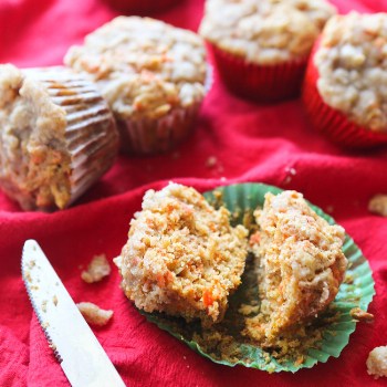 an apple carrot cake muffin split in half on a muffin wrapper with a butter knife next to it