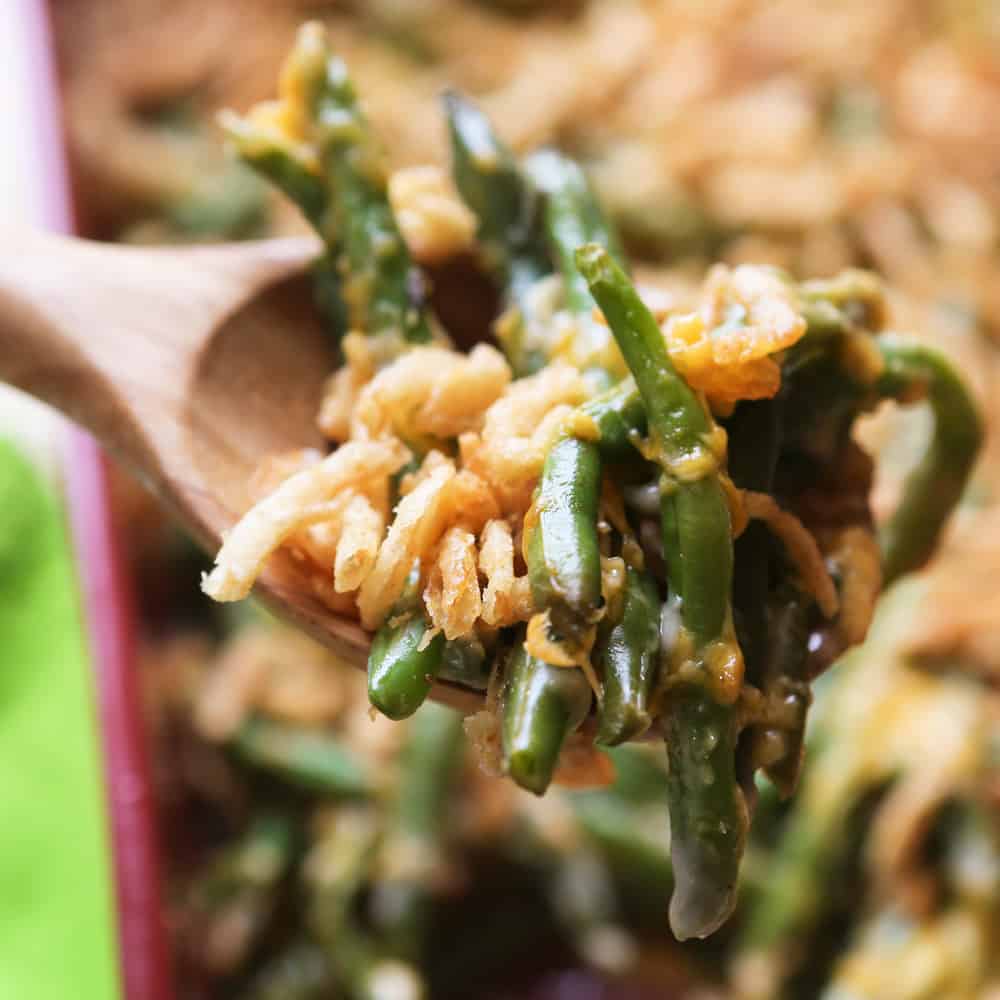 Wooden serving spoon full of green bean casserole over the casserole pan. 