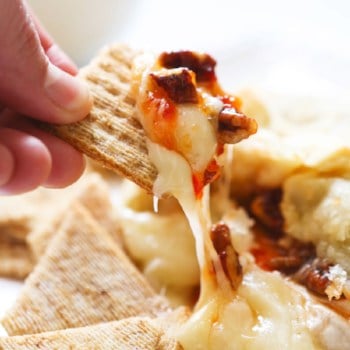 Triscuit cracker pulling cheesy bite from a plate, topped with pepper jam.