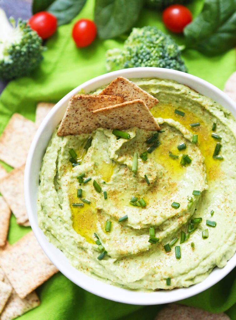 Wheat thin crackers tucked into a serving bowl of spinach hummus. 