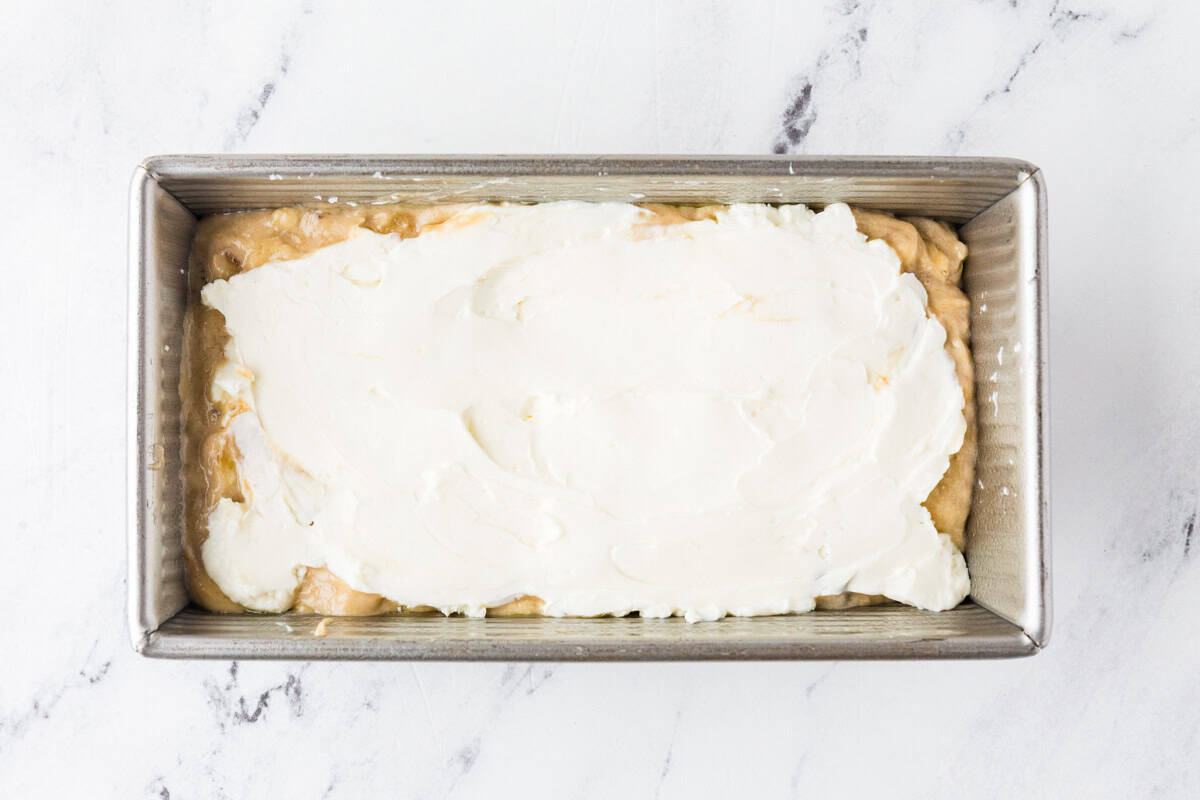Loaf pan with batter on bottom and a layer of cream cheese spread on top.