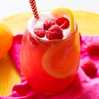 A full glass of a pink liquid with fresh raspberries on top.