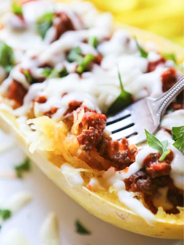 Fork removing cheesy, meaty bite out of cooked spaghetti squash.