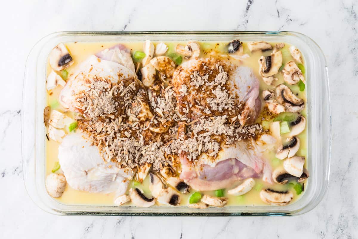 Top view of a glass baking dish filled with veggies, creamy sauce, chicken thighs and a dry mix sprinkled over top.