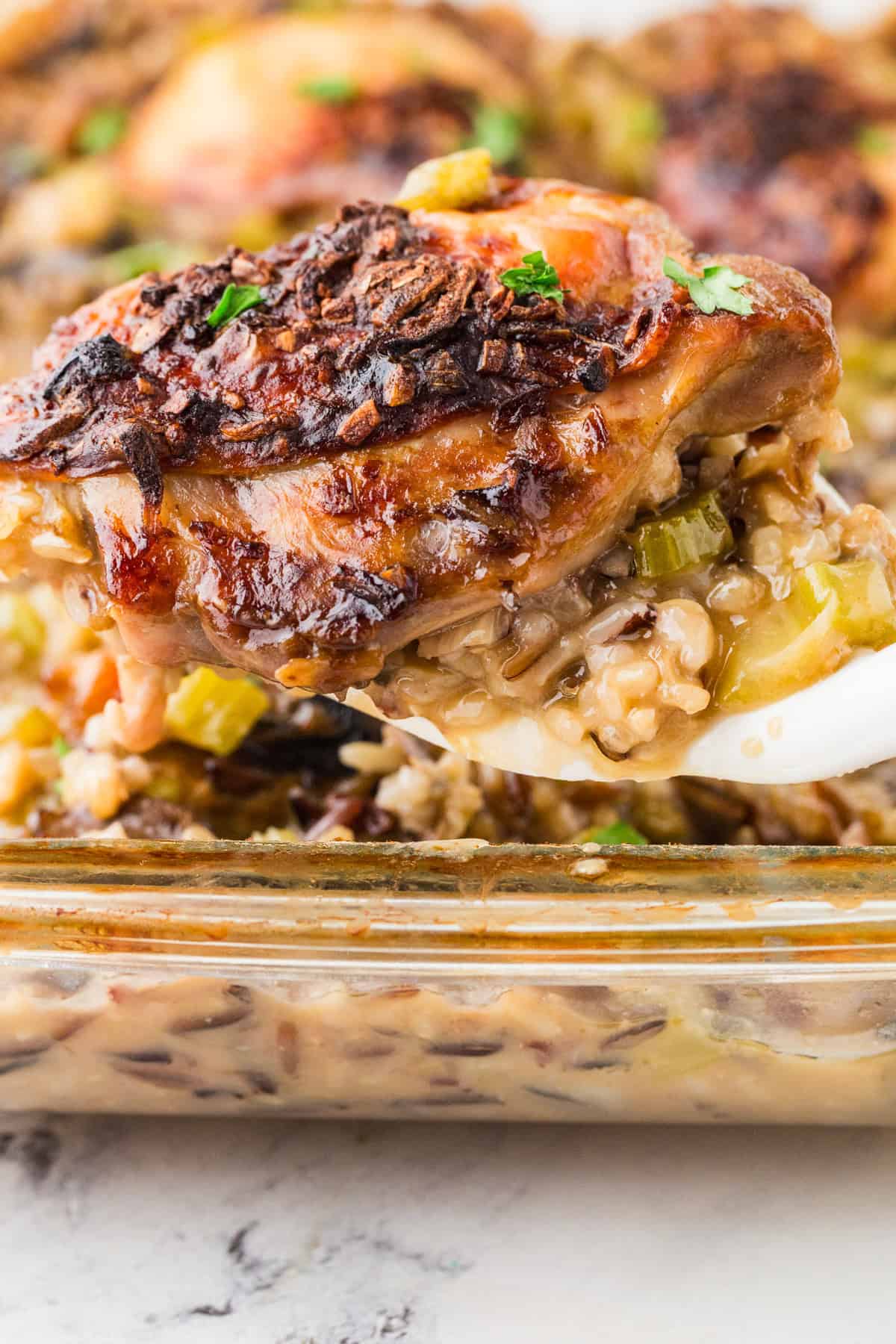 Spatula lifting a cooked chicken thigh out of a pan filled with rice and veggies.