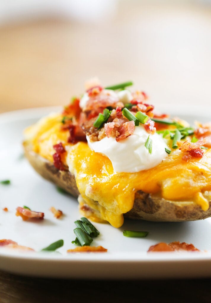 Twice baked potato topped with bacon and green onions on a plate. 