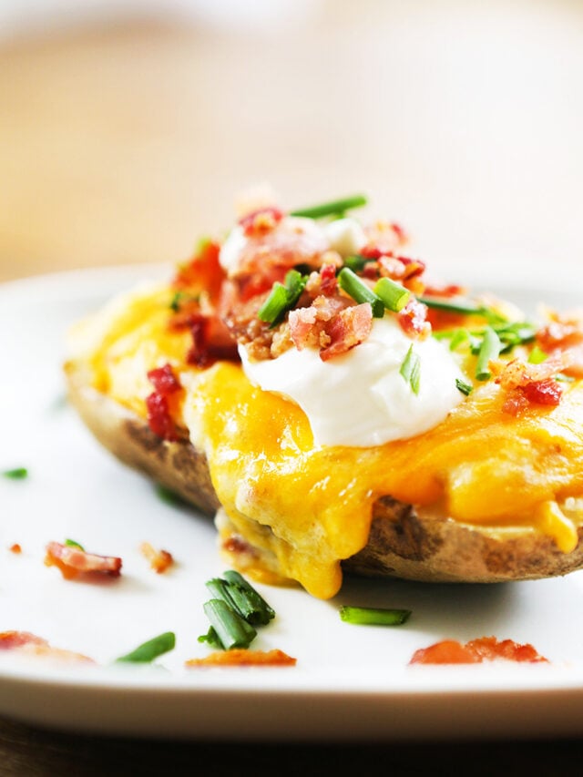 twice baked potato on a plate with sour cream and diced green onions and bacon over it. 
