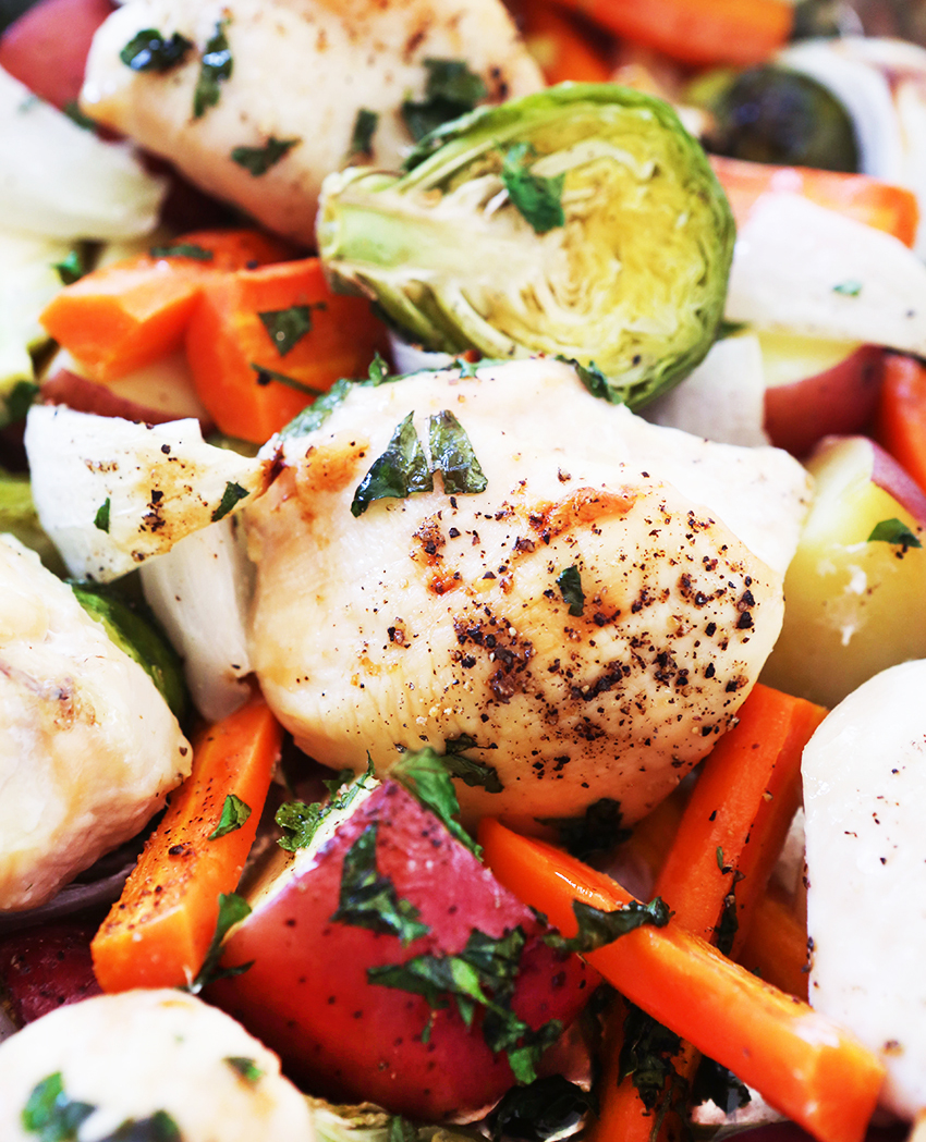 Roasted chicken pieces and vegetables with fresh herbs all piled together after being cooked.