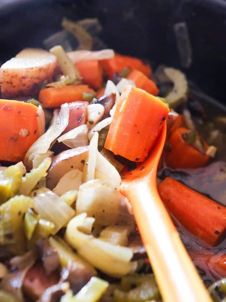 Spoon full of crockpot vegetables over the crock of prepared mixed vegetables