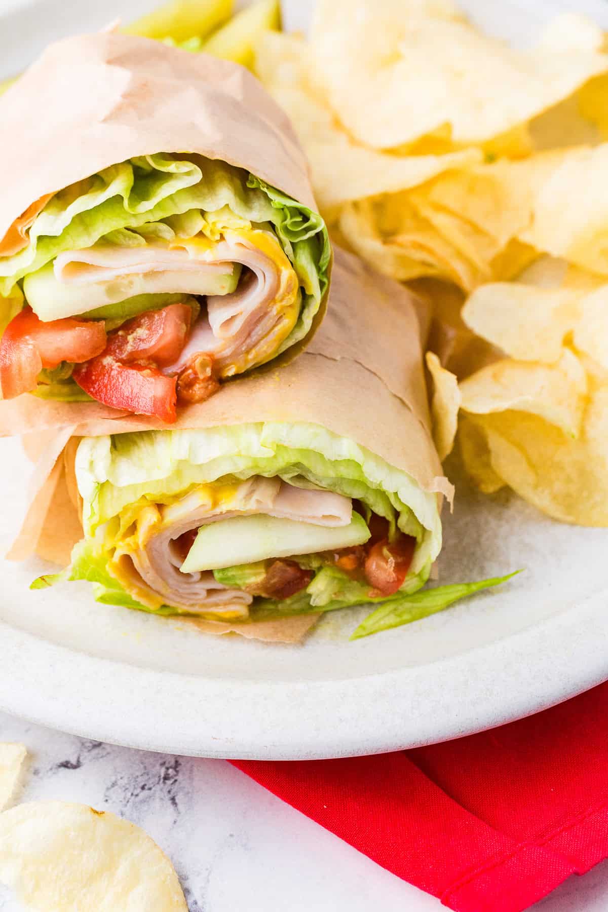 Unwich wrapped in parchment on a plate, next to a pile of chips.