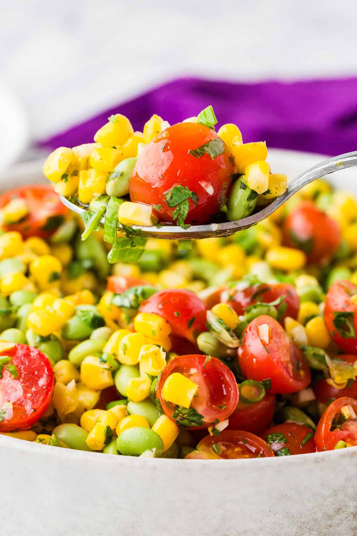 Spoon lifting tomato corn edamame salad out of a serving bowl filled with the mixture.