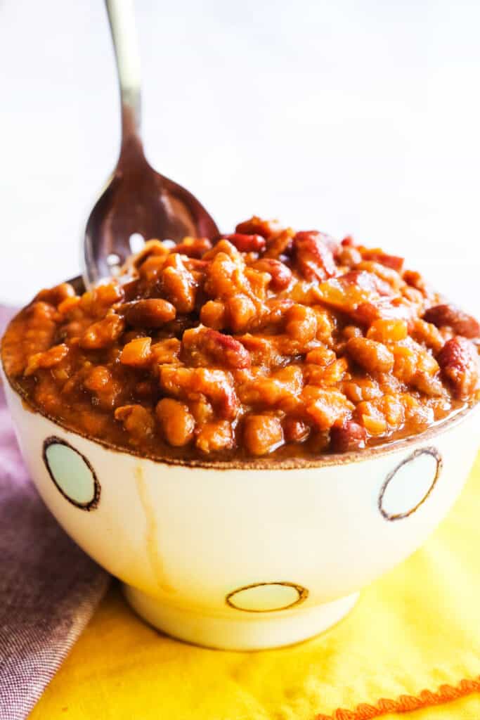 Crock pot baked beans in a bowl with a spoon tucked in. 