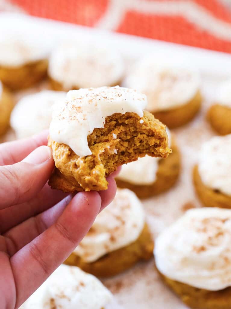 Hand holding up a soft pumpkin cookie with cream cheese topping. 