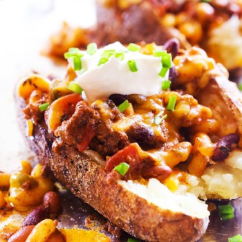 Baked potatoes cut in half with leftover chili topping them and a dollop of sour cream.