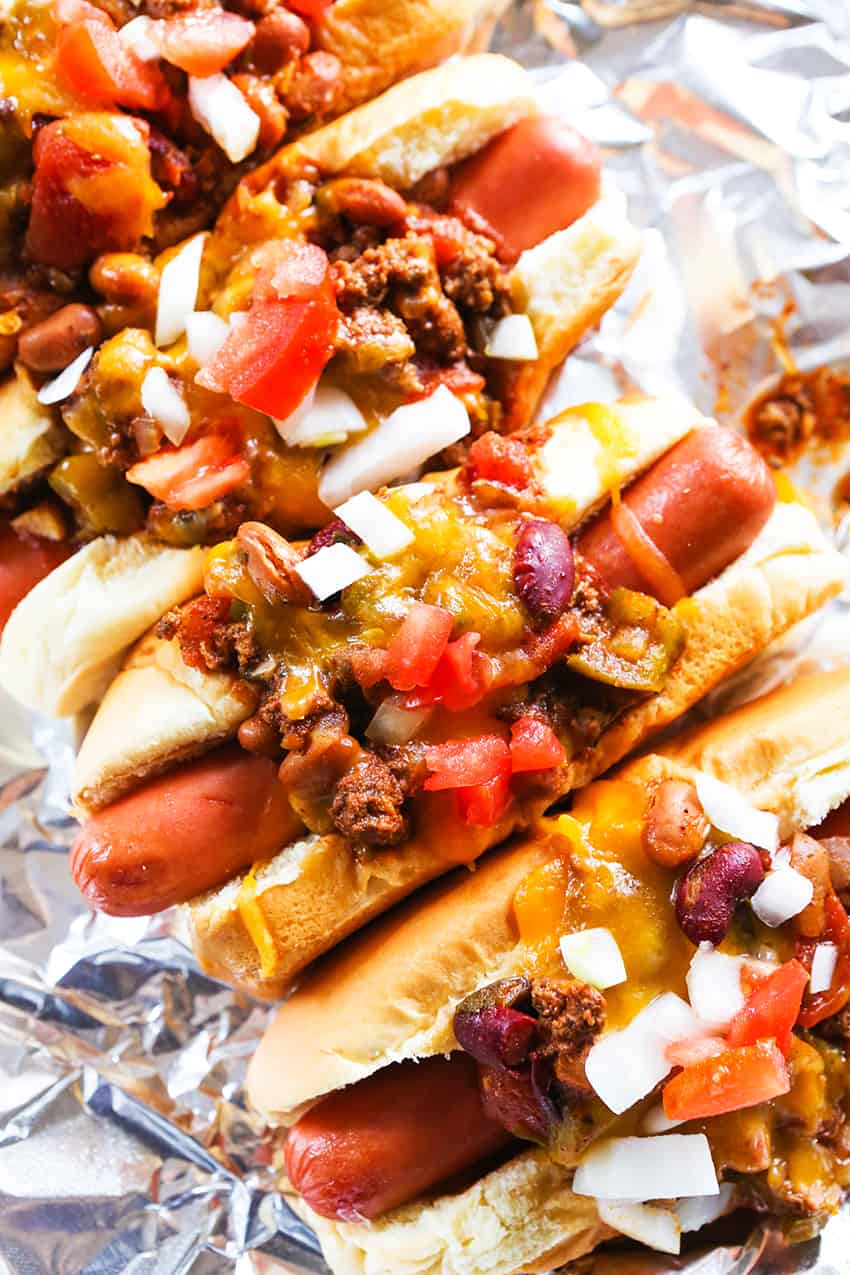 Chili dogs lined up on a sheet of foil in a row.