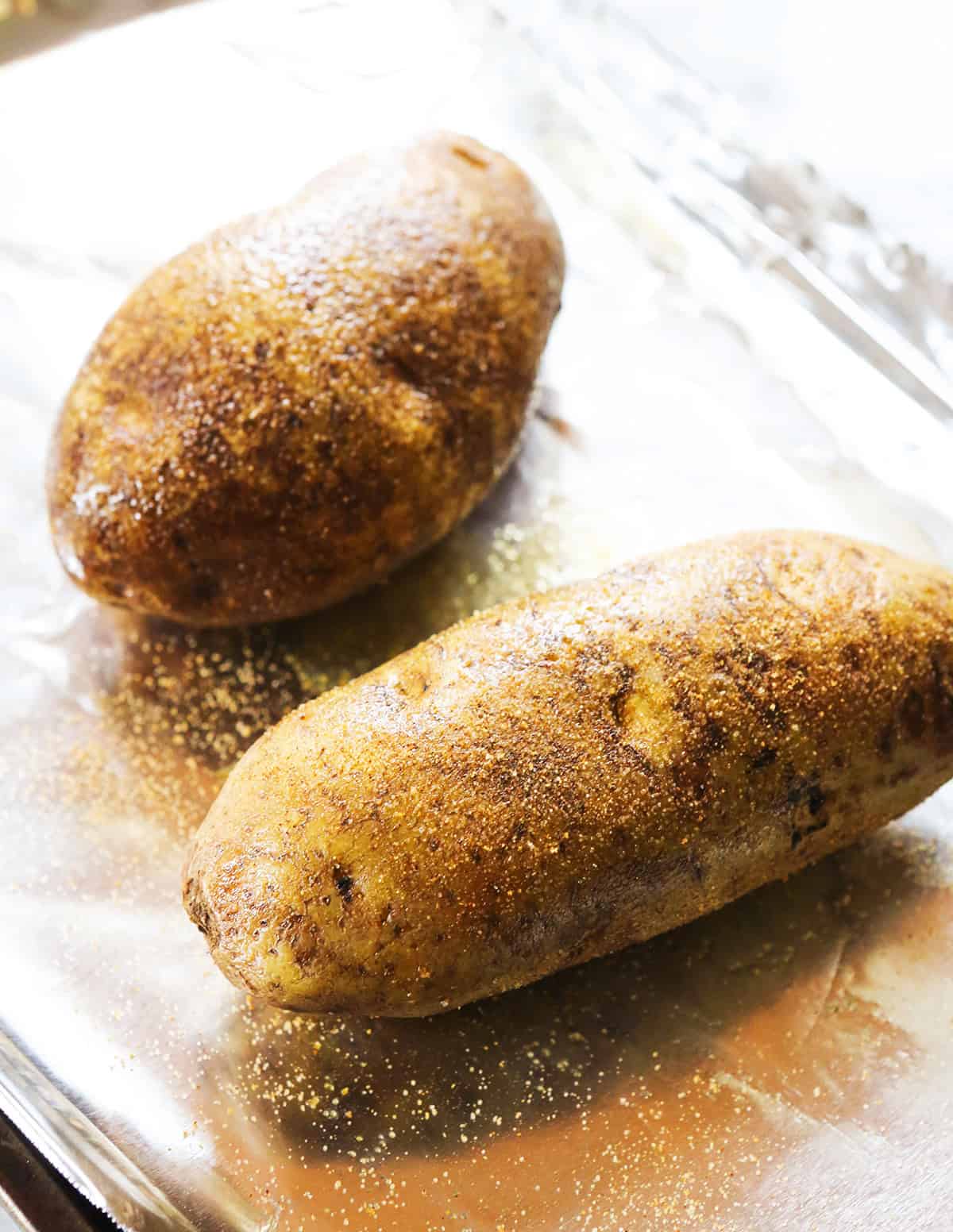 Two potatoes on foil, covered in seasoned salt.