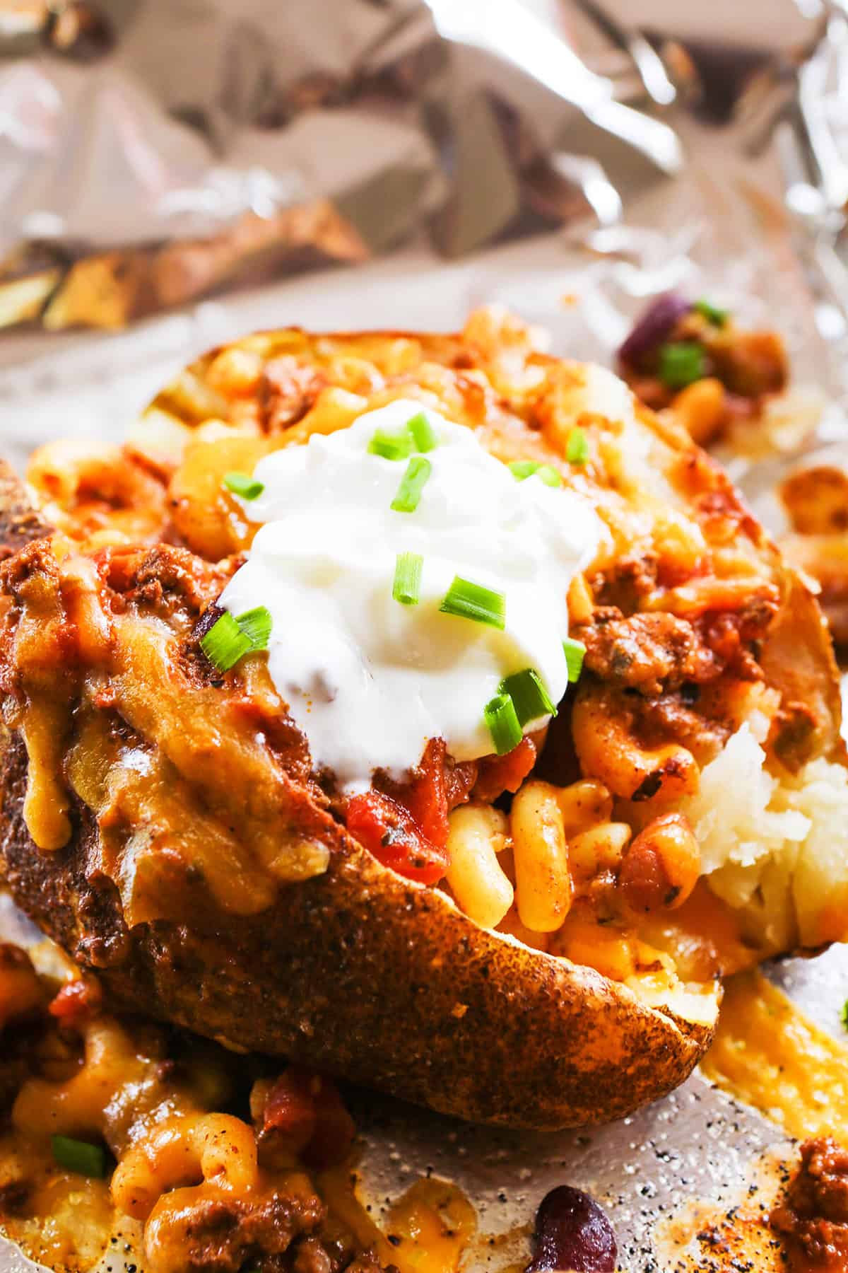 A fully loaded baked potato with chili, mac and cheese, sour cream and chives.