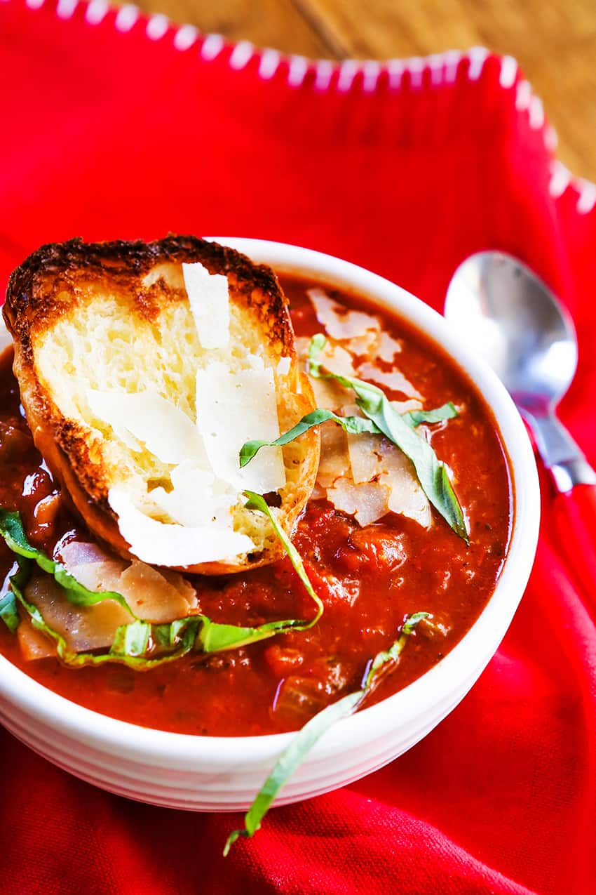 Bowl of tomato soup with broiled bread and basil on top.