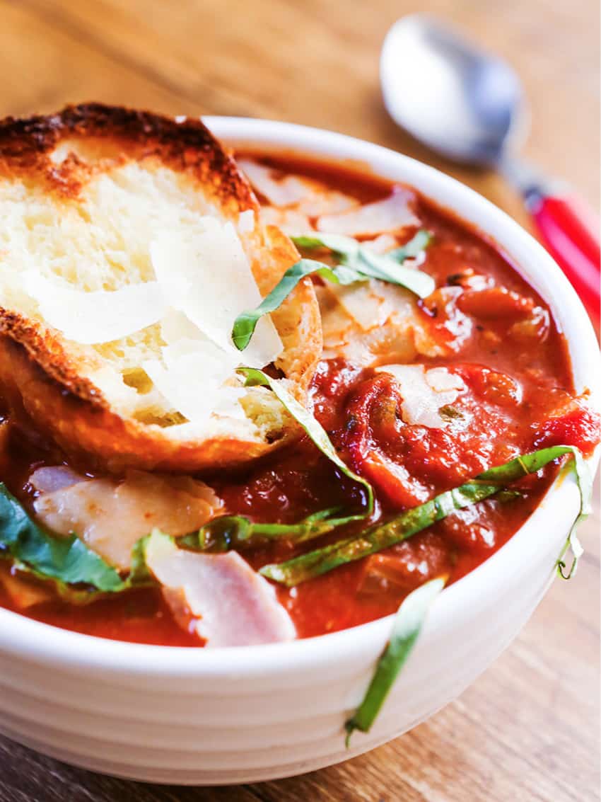 Bowl of heaping tomato soup topped with garlic bread and basil.