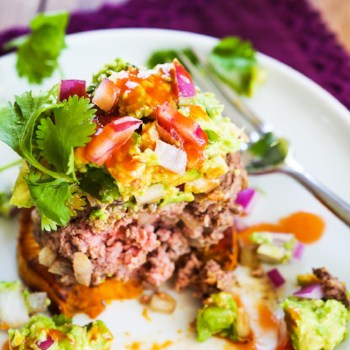 A healthy burger topped with avocado, hot sauce, cilantro sitting on a sweet potato as the bun.