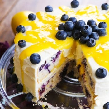 Lemon blueberry layered cake with lemon buttercream frosting and a slice removed from it.