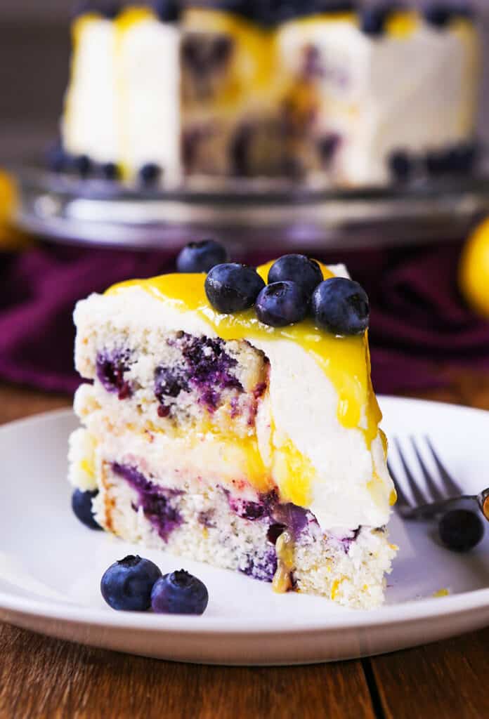 A slice of cake with blueberries and a a yellow glaze dripping down the sides.