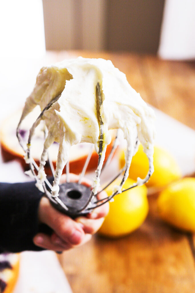 Hand holding a whisk filled with buttercream frosting.