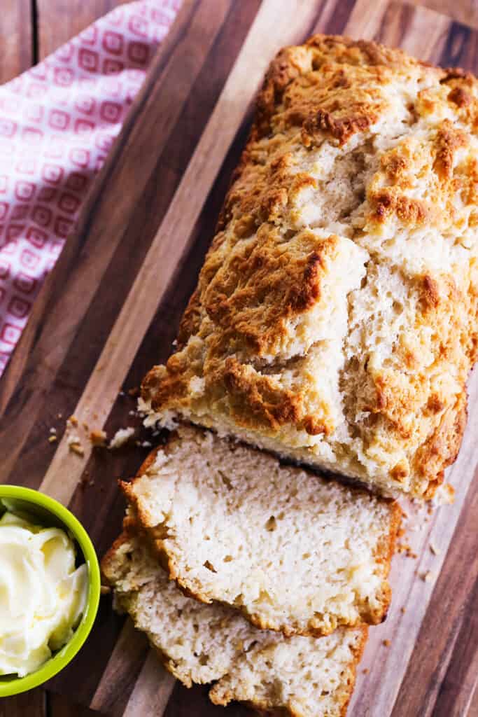 Beer bread on a cutting board with a couple slices falling down next to a pot of butter. 