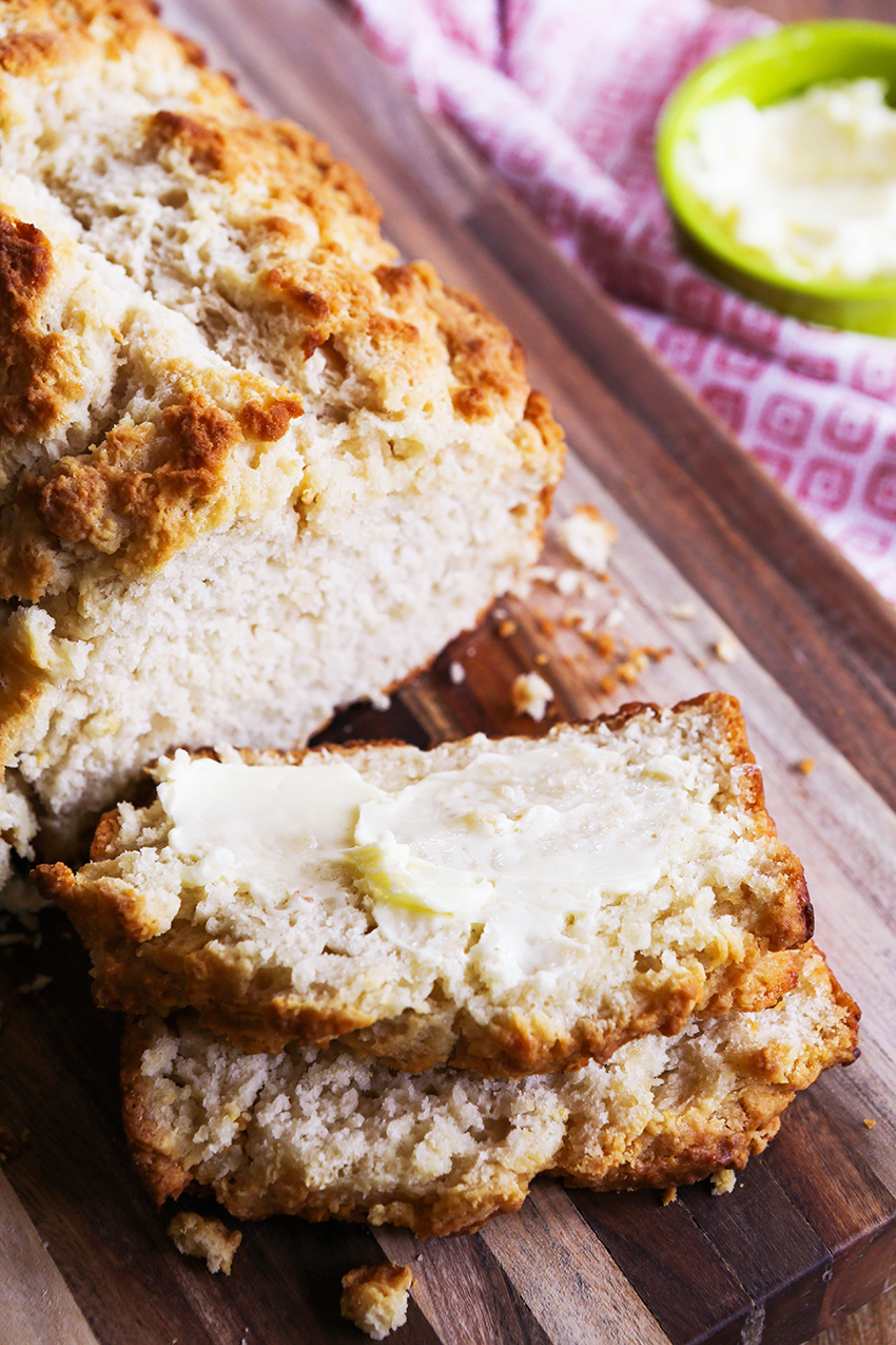 Loaf of no yeast beer bread with two slices cut away and one slathered in butter. 