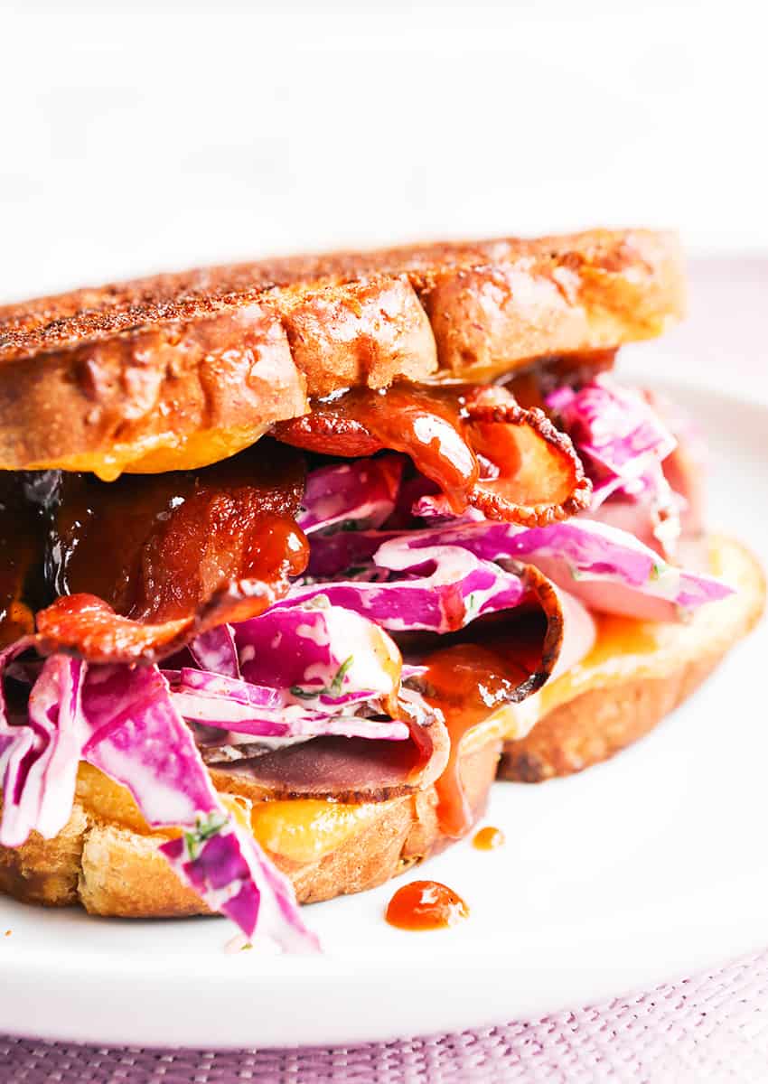 Side view of a grilled cheese sandwich overflowing with cabbage and bacon and sauce.