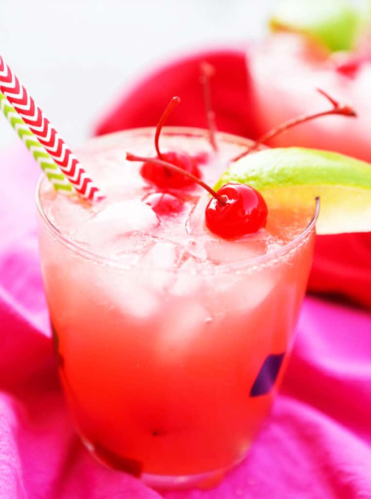 cherry limeade in a glass with a garnish of lime slice, cherries and two straws coming out