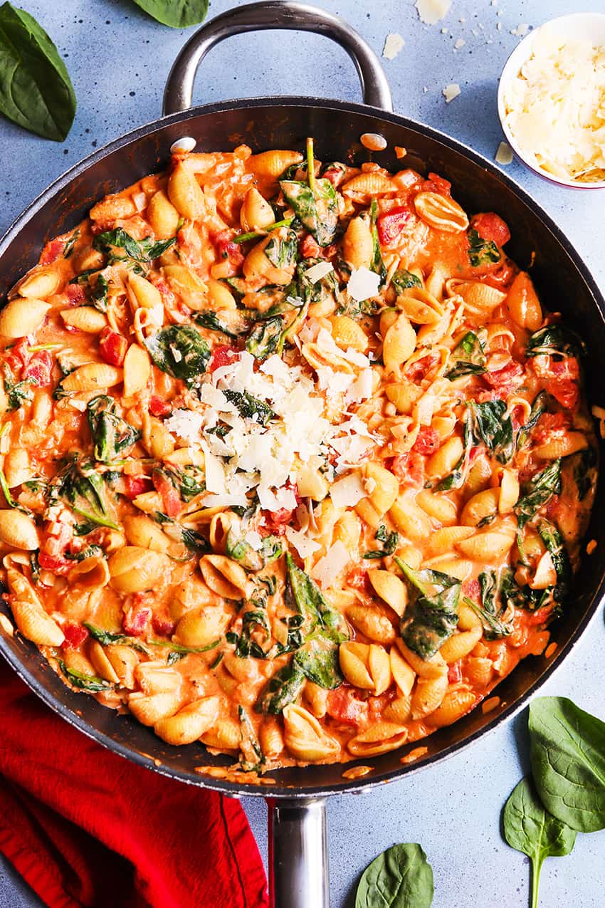 Skillet filled with cooked pasta shells, tomato sauce, spinach and cheese.