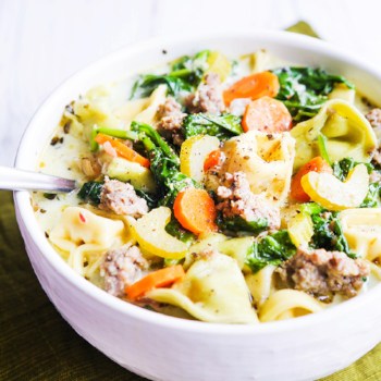 Bowl of tortellini soup with a spoon tucked into it. 